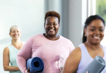 three women smile after yoga class holding their mats and water