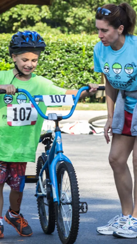 Parent helping a child on a bike during a triathlon