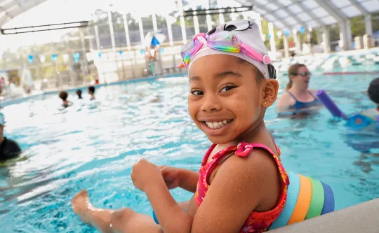 A preschooler with goggles and floties eagerly waits her turn for swim lessons