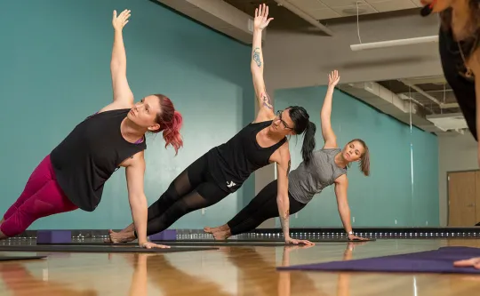 several women hold a side plan in a YMCA yoga class