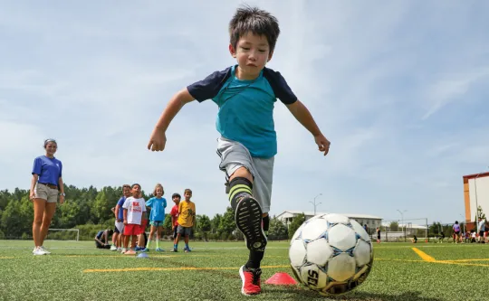 Young boy kicking soccer ball toward a goal