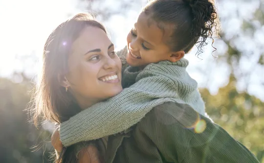 Image of smiling mother and daughter outside on a sunny day.