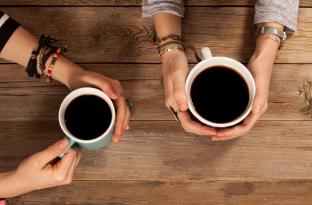 hands holding coffee cups at a table