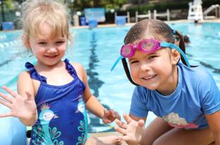 Two small girls wading in the shallow pool water and waving