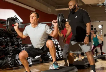 an instructor spots a member lifting a barbell