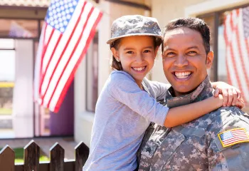 a military parent holds a child in front of American flag