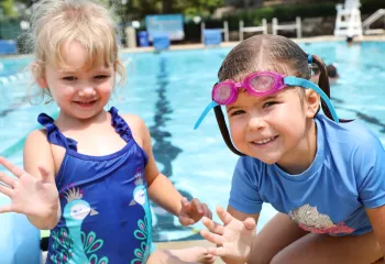 Two small girls wading in the shallow pool water and waving