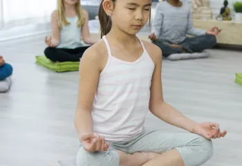 Children sitting on mat and floor in a seated yoga meditation position