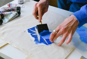 blue paint being painted on a tote bag with a stencil 