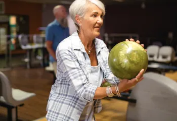 close up shot of woman with green bowling ball in stance about to take a turn rolling