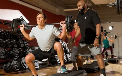 an instructor spots a member lifting a barbell