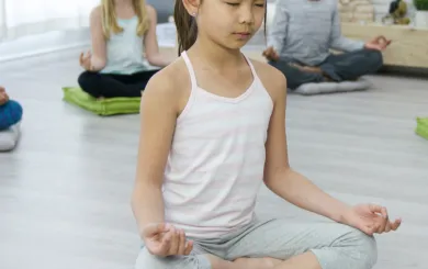 Children sitting on mat and floor in a seated yoga meditation position
