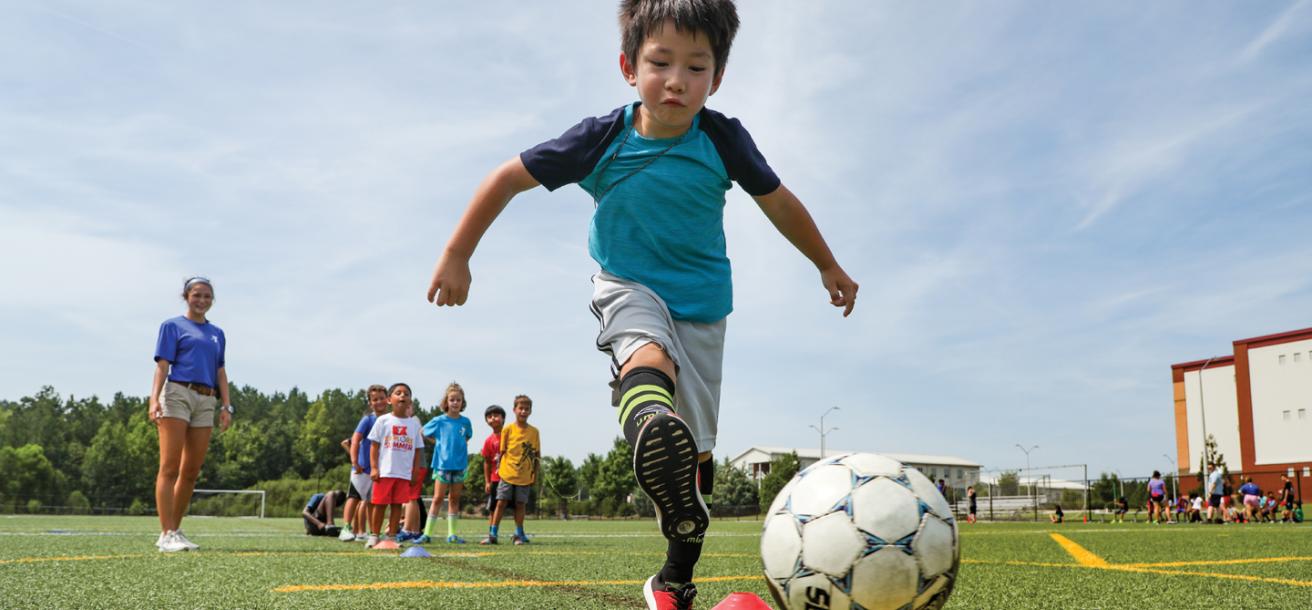 Young boy kicking soccer ball toward a goal