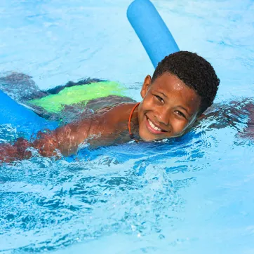 Young boy swimming with a pool noodle 