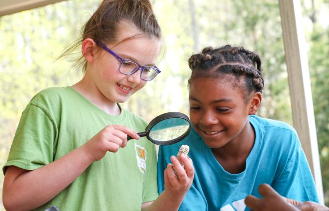 Two girls looking at a fossil with a magnifying glass