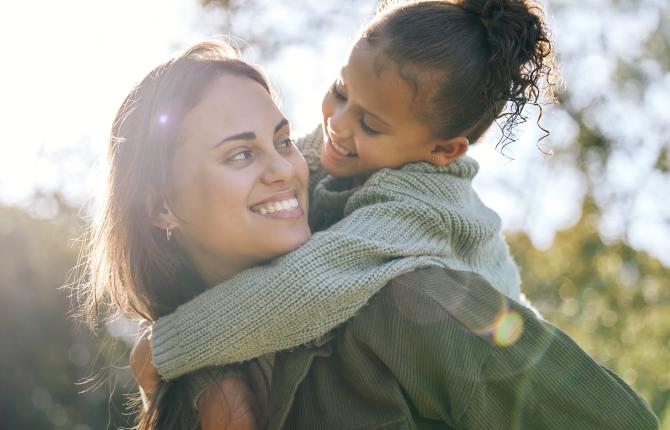 Image of smiling mother and daughter outside on a sunny day.